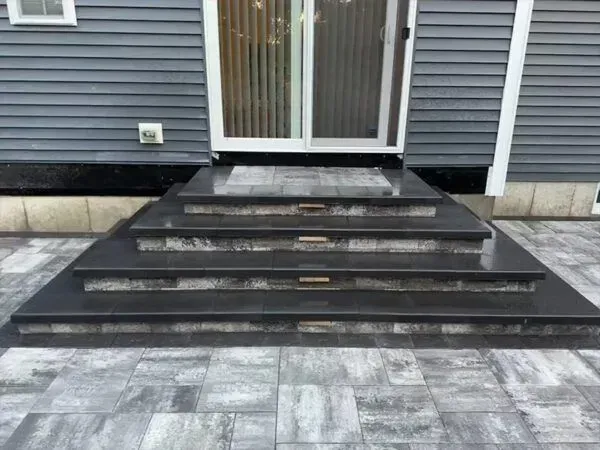 Gray stone steps leading to a sliding glass door; the steps and patio are gray, and the house siding is blue.