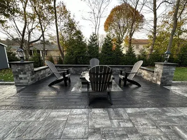 Patio with Adirondack chairs around a fire pit, surrounded by a stone wall and landscaping.