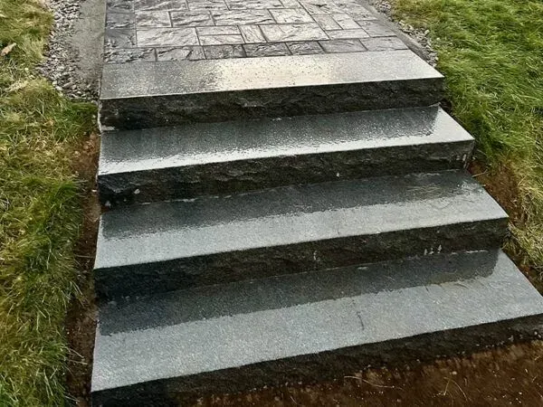 Granite steps leading up to a stone walkway, surrounded by green grass.