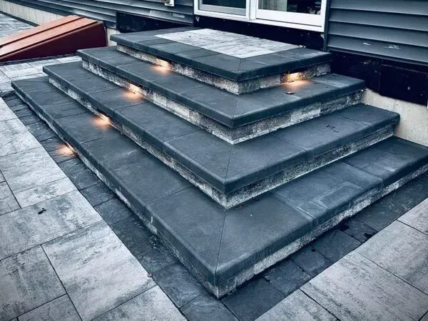 Stone steps with integrated lighting leading to a doorway, set in a paved patio.