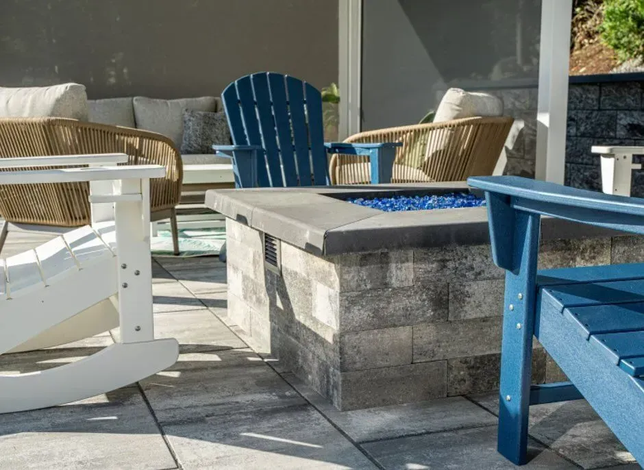 Patio with fire pit, blue and white Adirondack chairs, and woven seating.