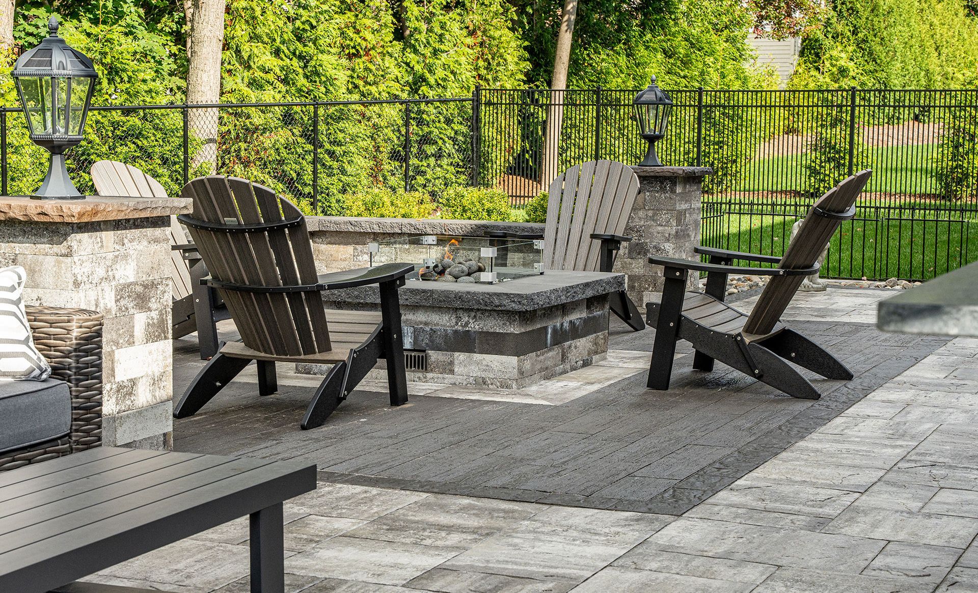 Outdoor seating area with Adirondack chairs around a fire pit on a stone patio.