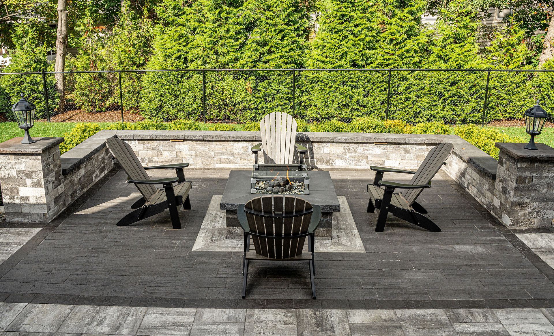 Patio with Adirondack chairs around a fire pit, surrounded by a stone wall and greenery.