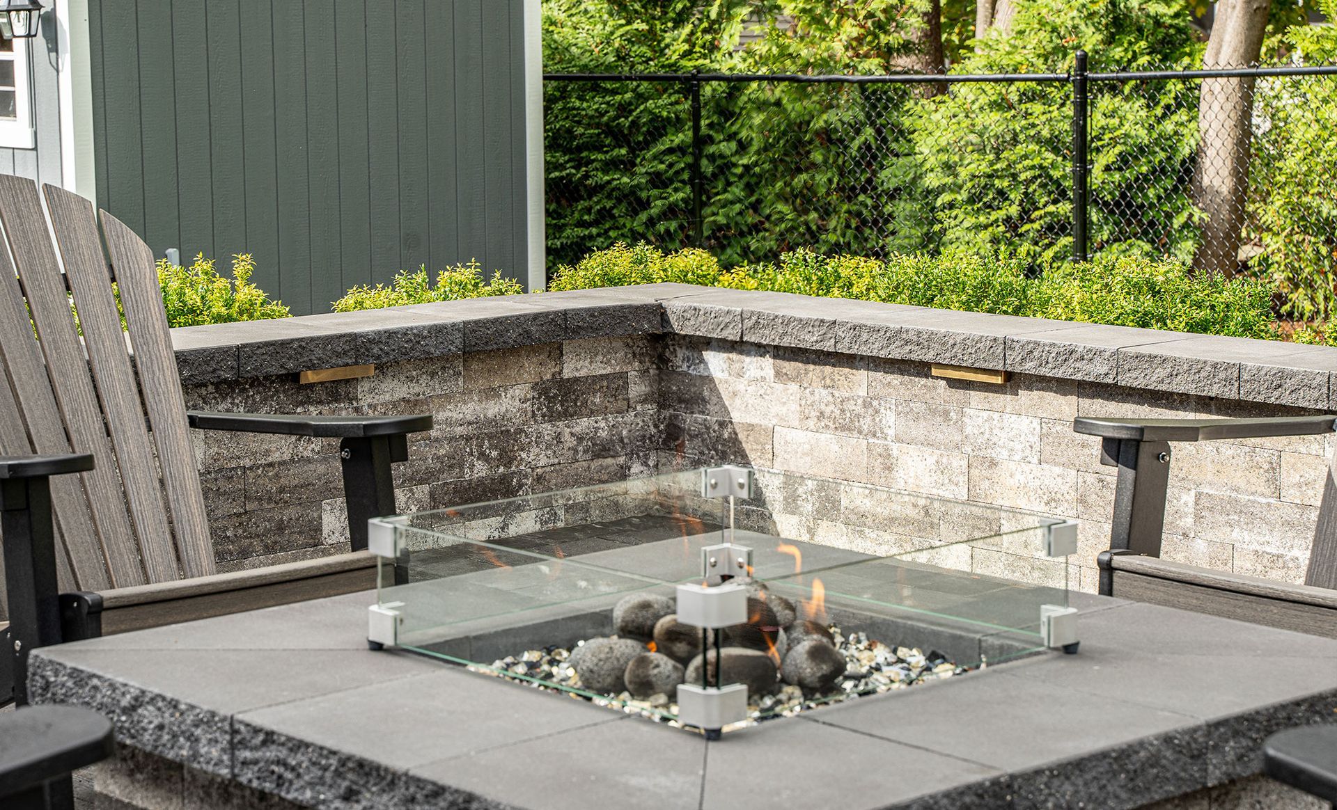 Square stone fire pit with glass wind guard, surrounded by built-in stone seating.