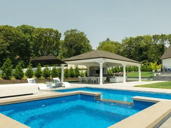 Pool with gazebo, lounge chairs, and manicured landscaping, bright blue water, sunny day.