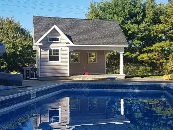 Pool house next to a pool with a blue tiled bottom. Exterior has a covered porch with white columns.