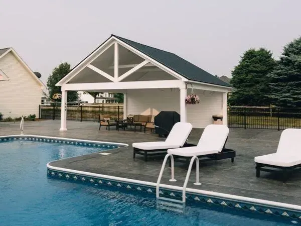 Poolside cabana with lounge chairs, blue pool, white structure, and black roof.