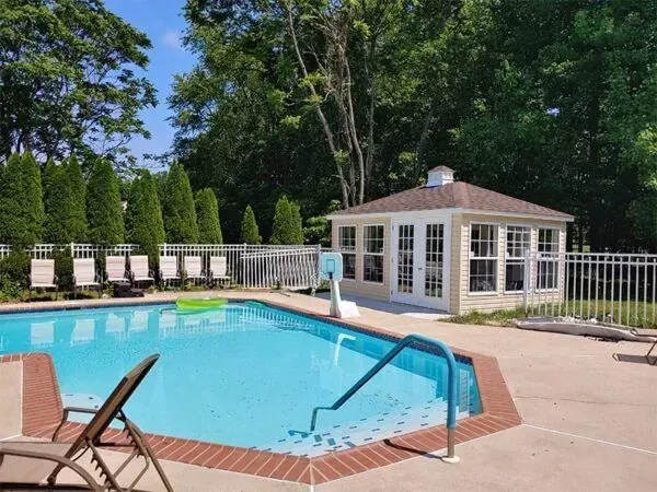 Swimming pool with gazebo, lounge chairs, and fencing. Bright blue water, sunny day.