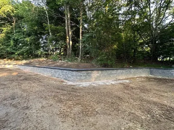Stone retaining wall along a dirt path, with trees in the background.
