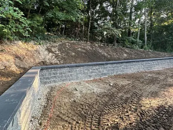Gray retaining wall built into a hillside, with excavated dirt and trees in the background.