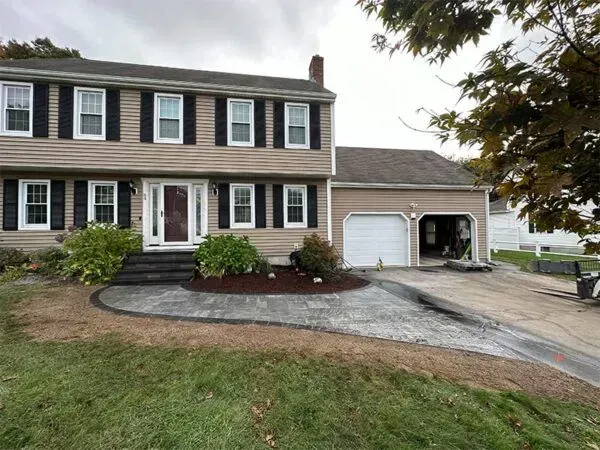 Two-story beige house with black shutters, steps, and a paved walkway leading to the driveway and garage.