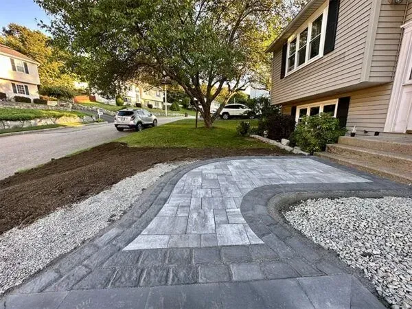 Gray paver walkway curving towards a beige house with gravel and mulch landscaping.