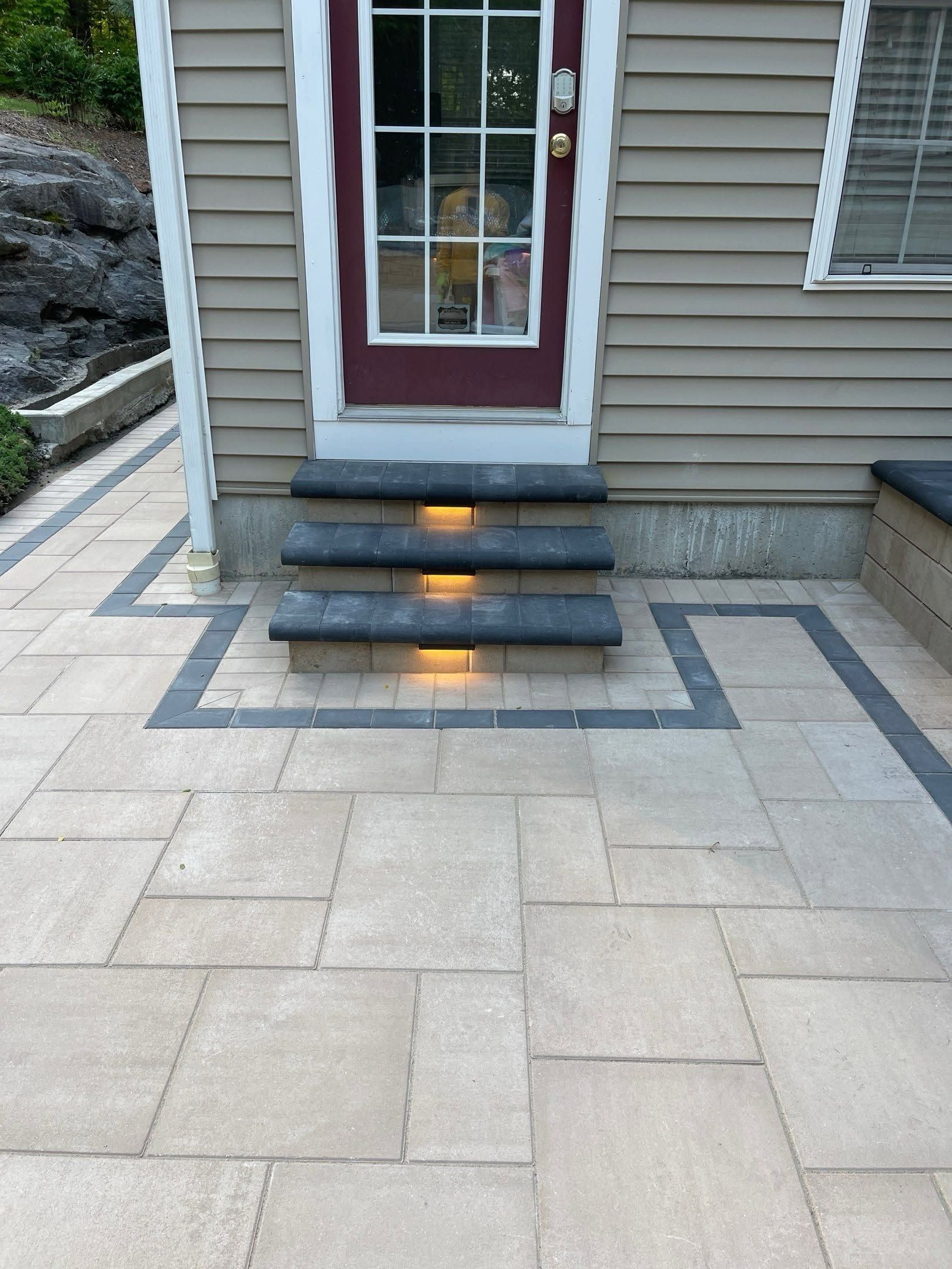 Front steps with lit stair lights leading to a white-framed glass door on a paved patio