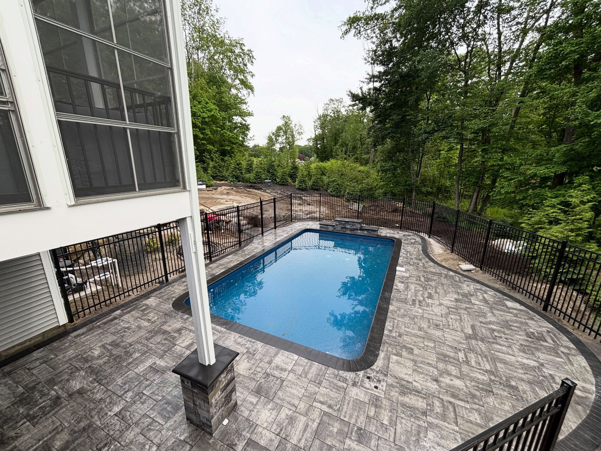 Backyard pool beside a house, with black fence and surrounding trees