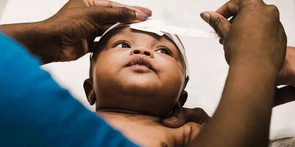 Adult hands lift a baby’s shirt to examine the chest against a plain background.