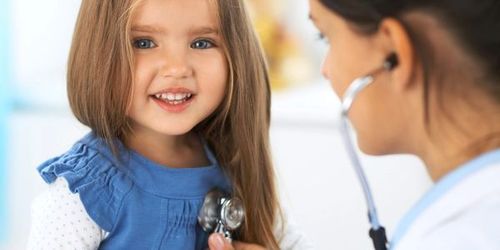 Doctor examining a smiling child with a stethoscope in a clinic