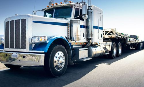 White-and-blue semi-truck hauling a long flatbed trailer on a sunny road