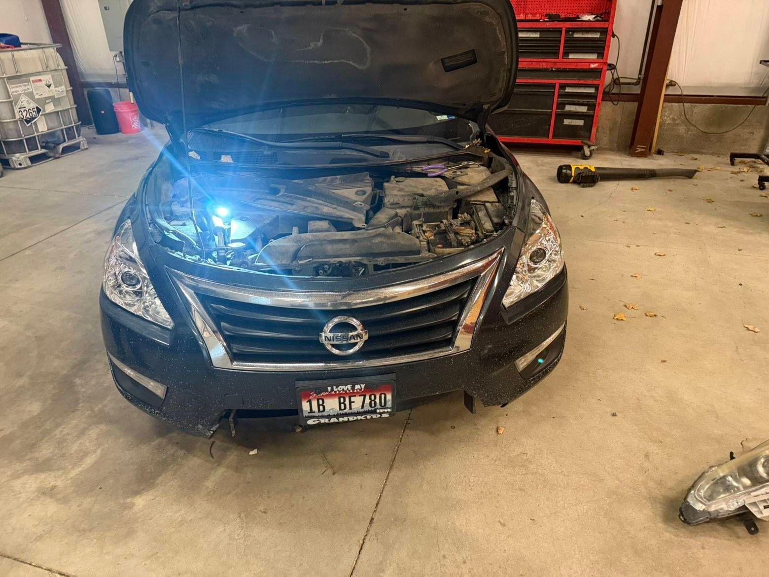 Black Nissan with hood open in a garage, front left headlight shining bright blue