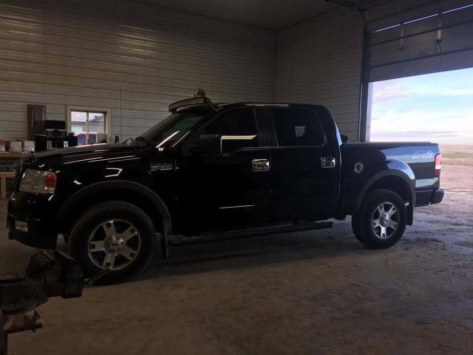 Black pickup truck parked inside a garage bay with the door open to daylight