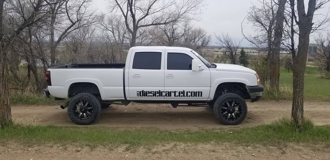 White lifted pickup truck parked on a dirt road with trees in the background
