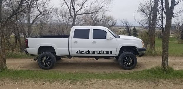 White lifted pickup truck parked on a dirt road with bare trees in the background