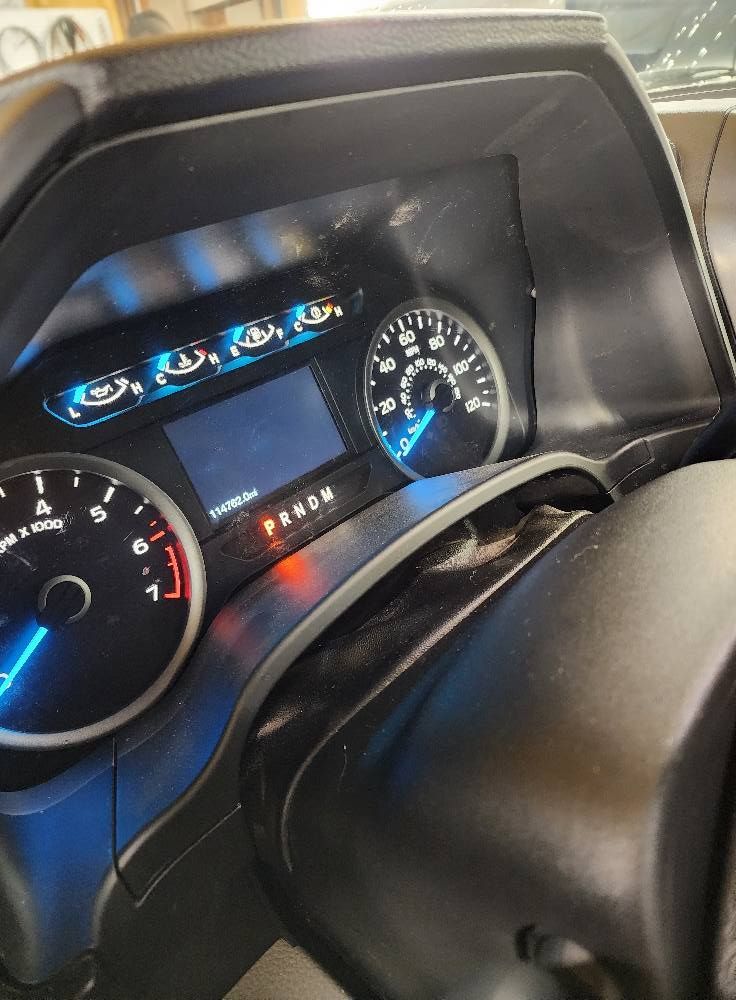 Car dashboard with illuminated speedometer, gauges, and center display behind the steering wheel.