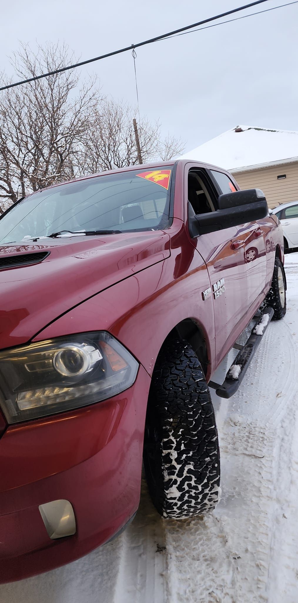 Red pickup truck parked in a snowy lot, front-left view with headlights on.