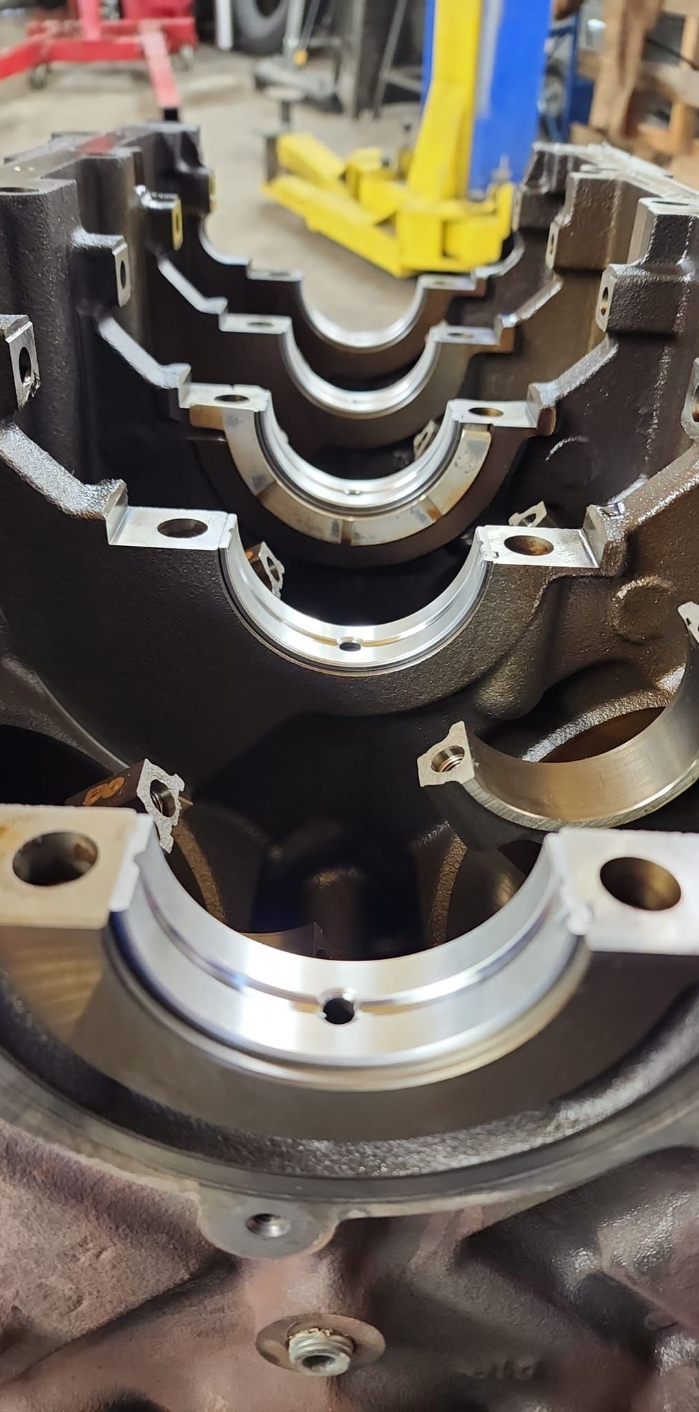 Close-up of a metal engine assembly with yellow tool inserting parts into stacked bearing shells
