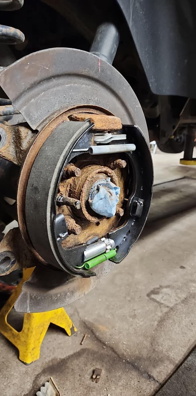 Close-up of a rusty brake rotor and wheel hub on a car lifted with a yellow jack stand.