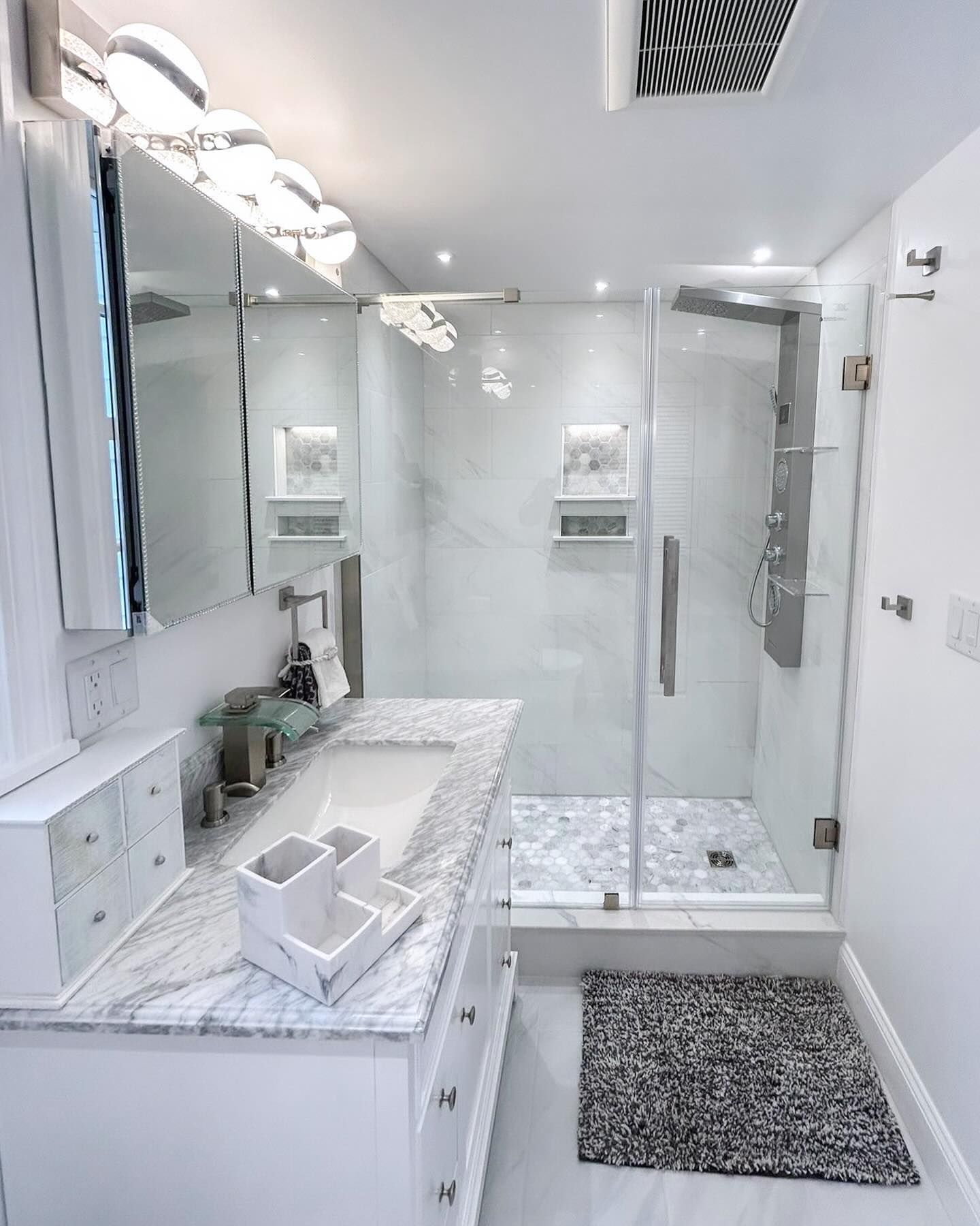 Bright white bathroom with double vanity, large mirror, glass shower, and gray rug