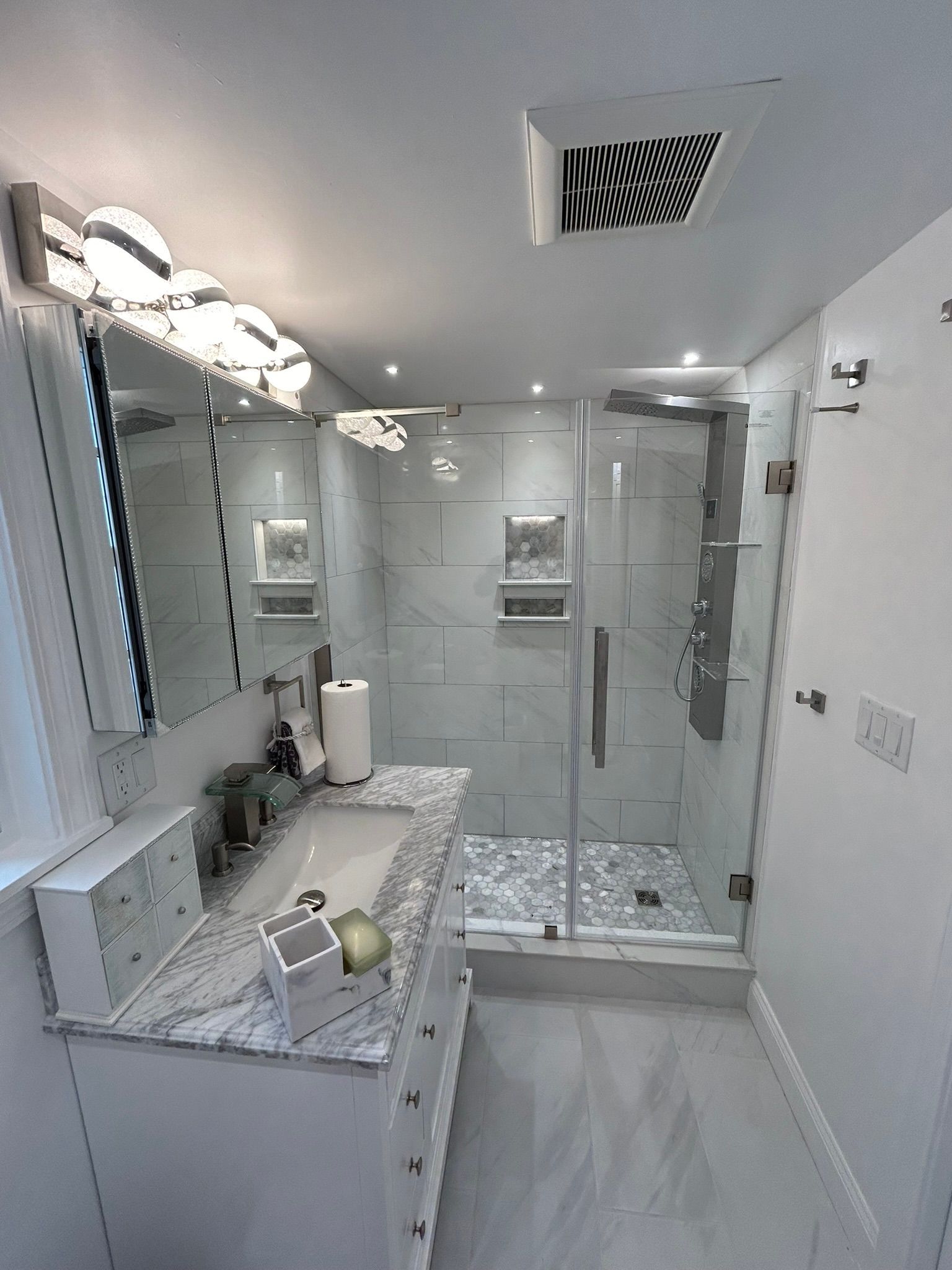 Bright modern bathroom with walk-in glass shower, vanity, and white marble tile.