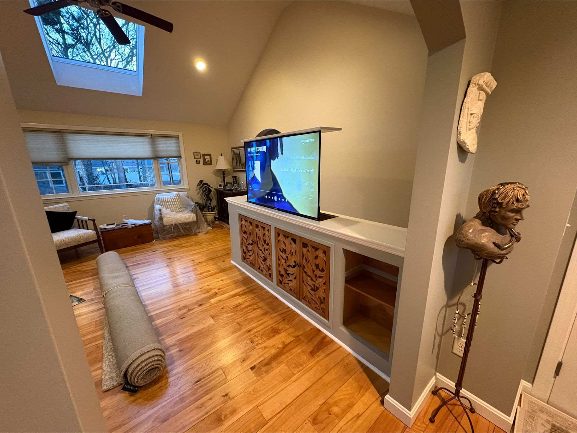 Living room with hardwood floors, a large TV, sectional sofa, and a skylight ceiling