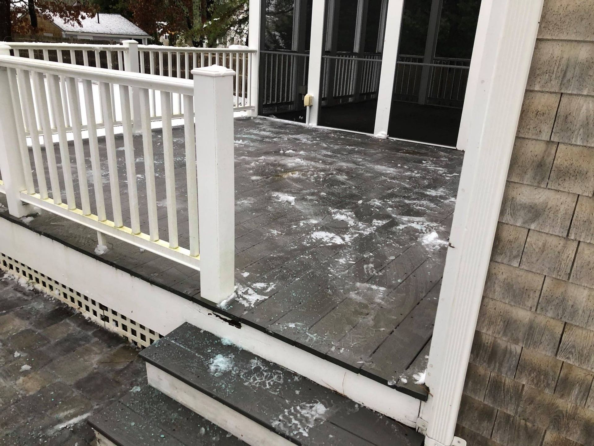 Snowy deck with white railing, gray decking, steps, and house siding.