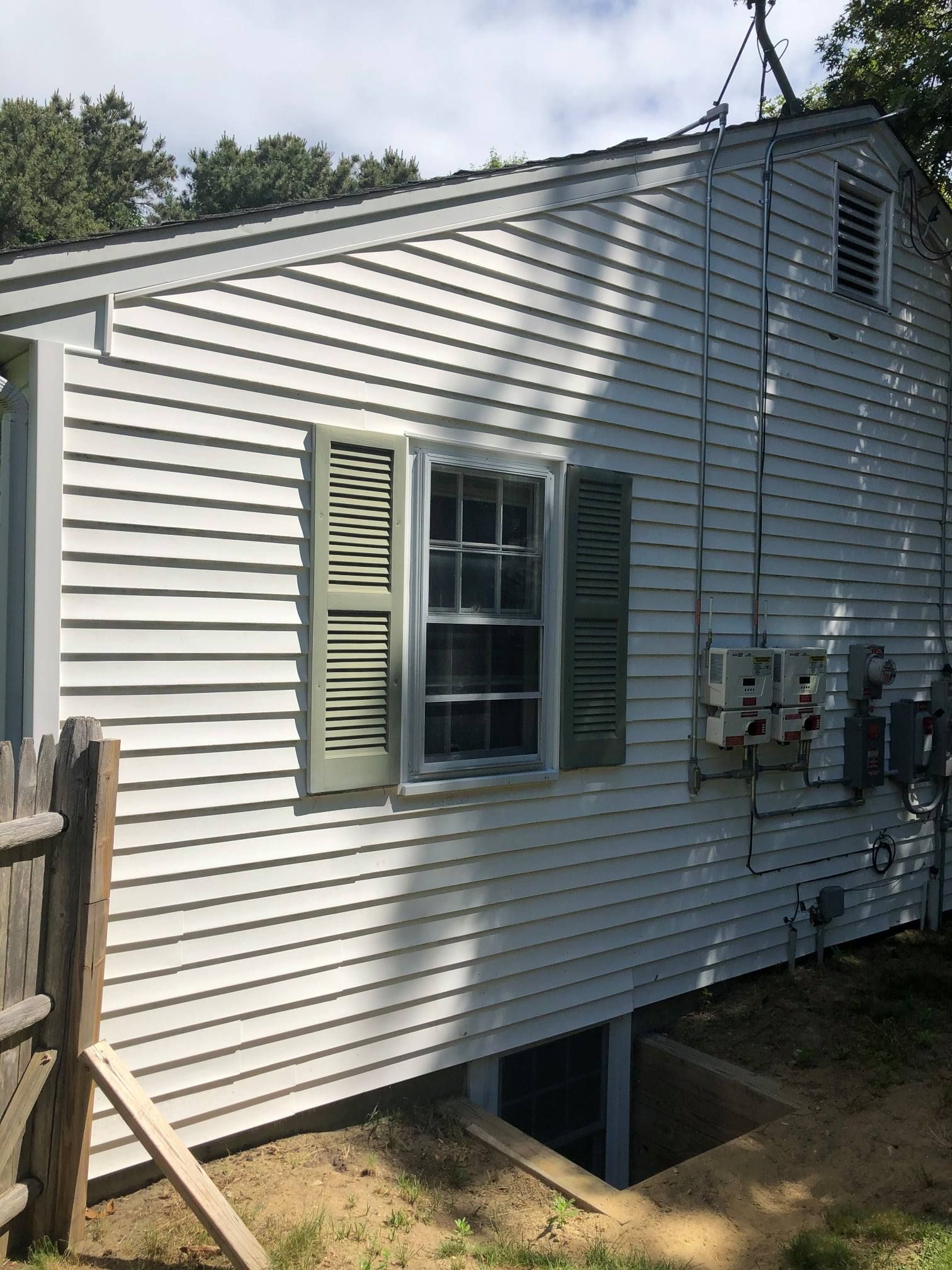White clapboard house with green shutters, window, and basement entrance.