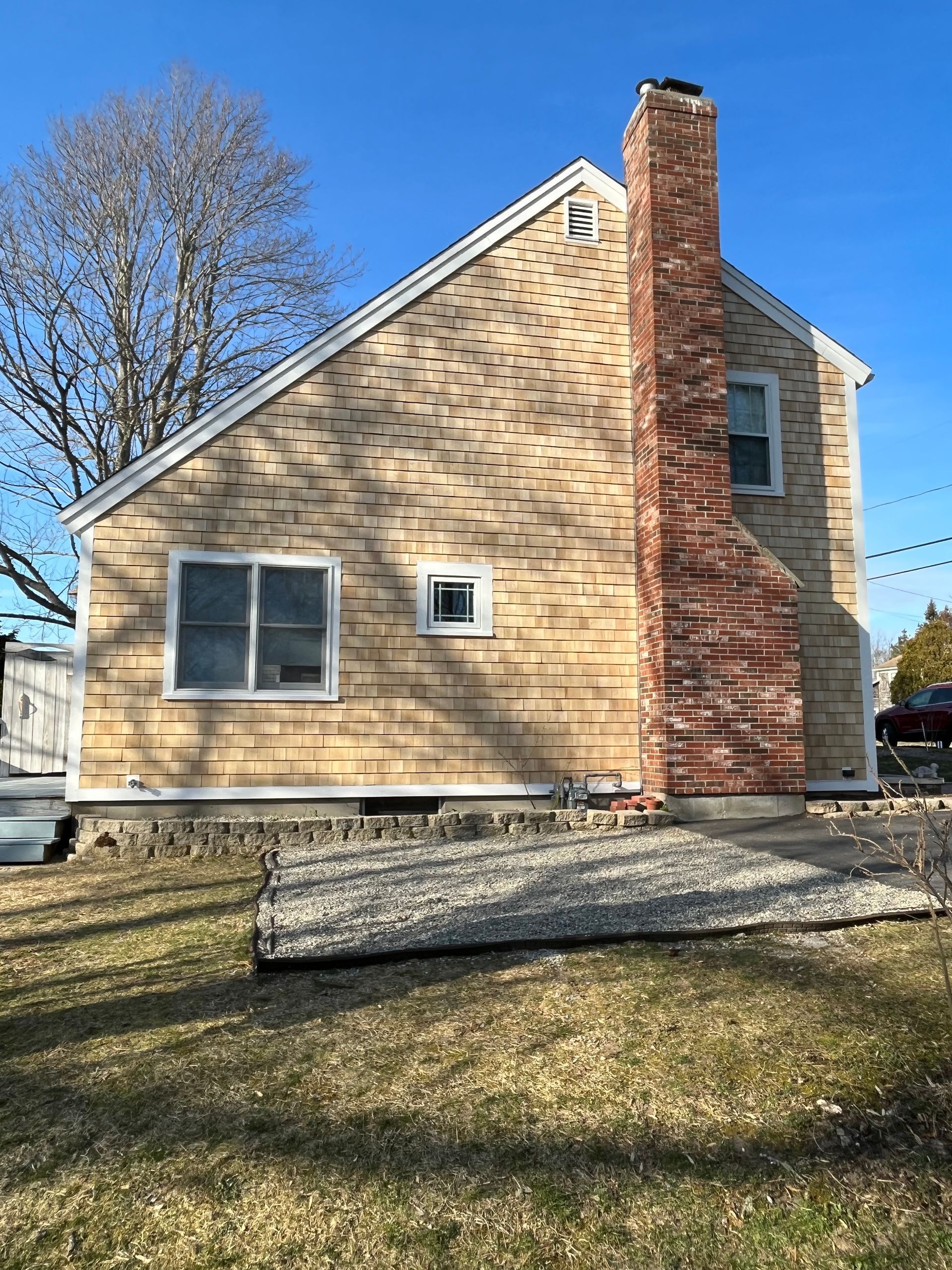 Side view of a house with tan siding and a tall brick chimney against a blue sky.