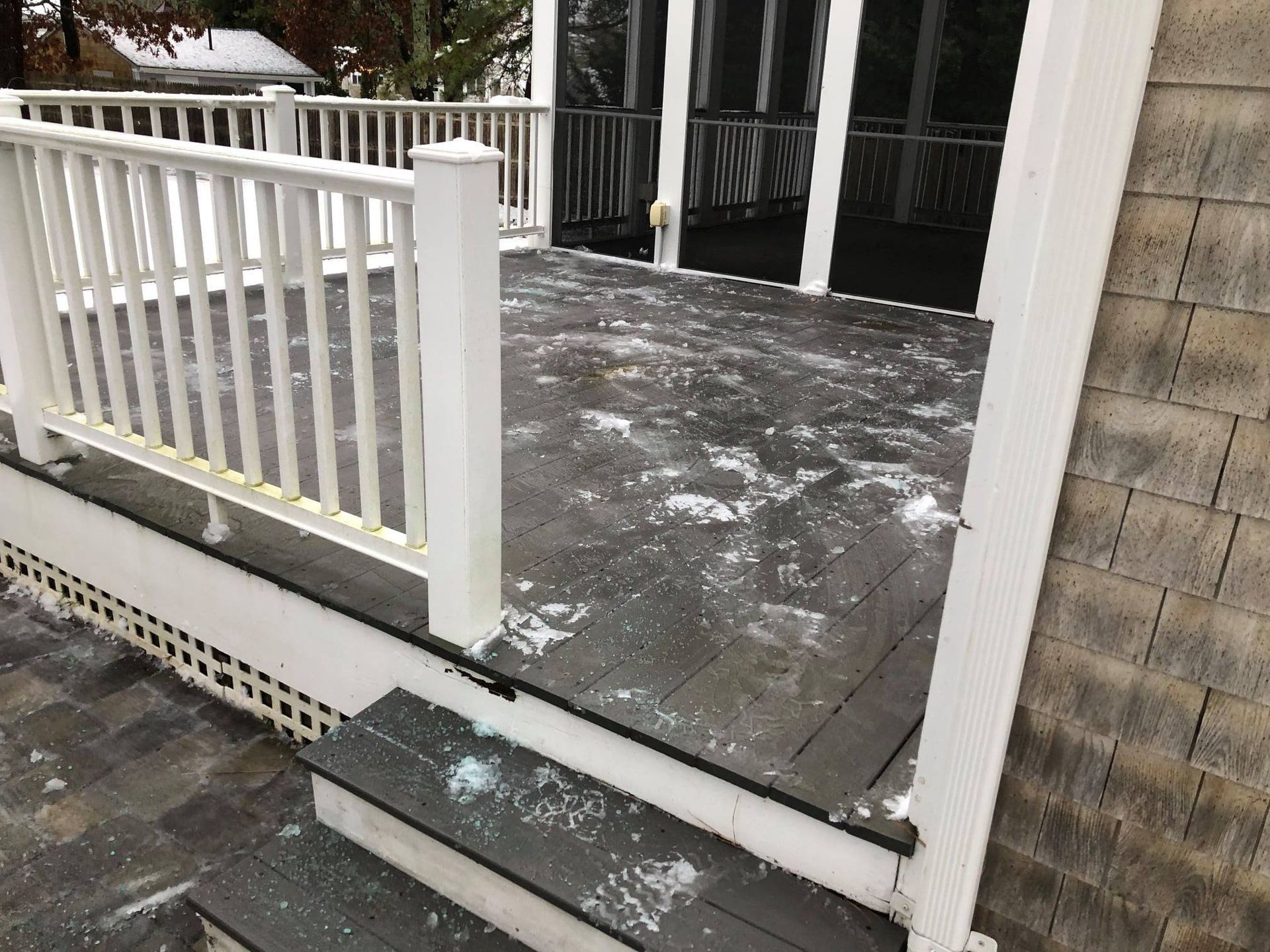Snow-dusted wooden porch with white railings and screened doors beside a stone wall