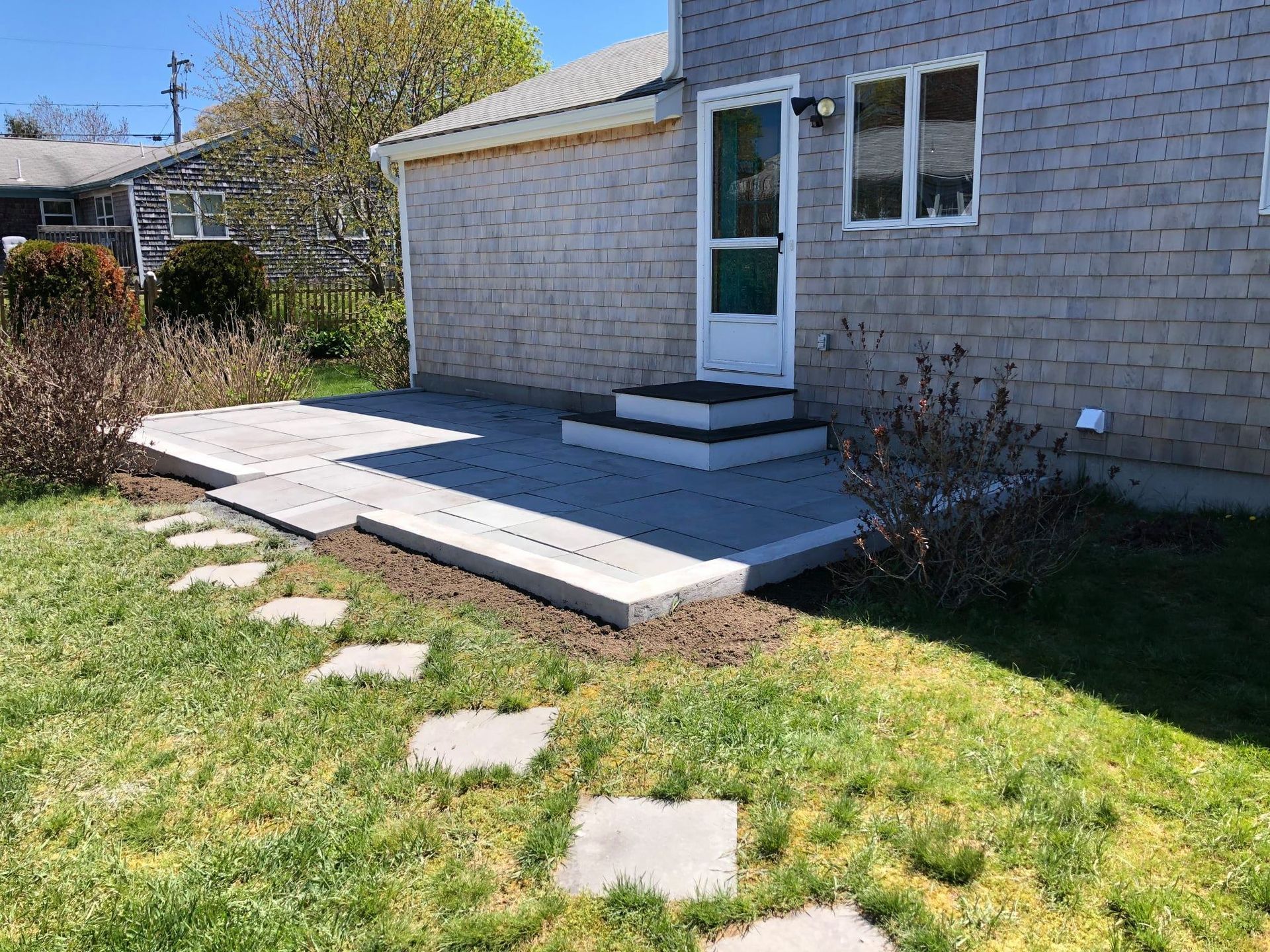 Backyard deck and steps beside a house, with stepping stones in the grass.