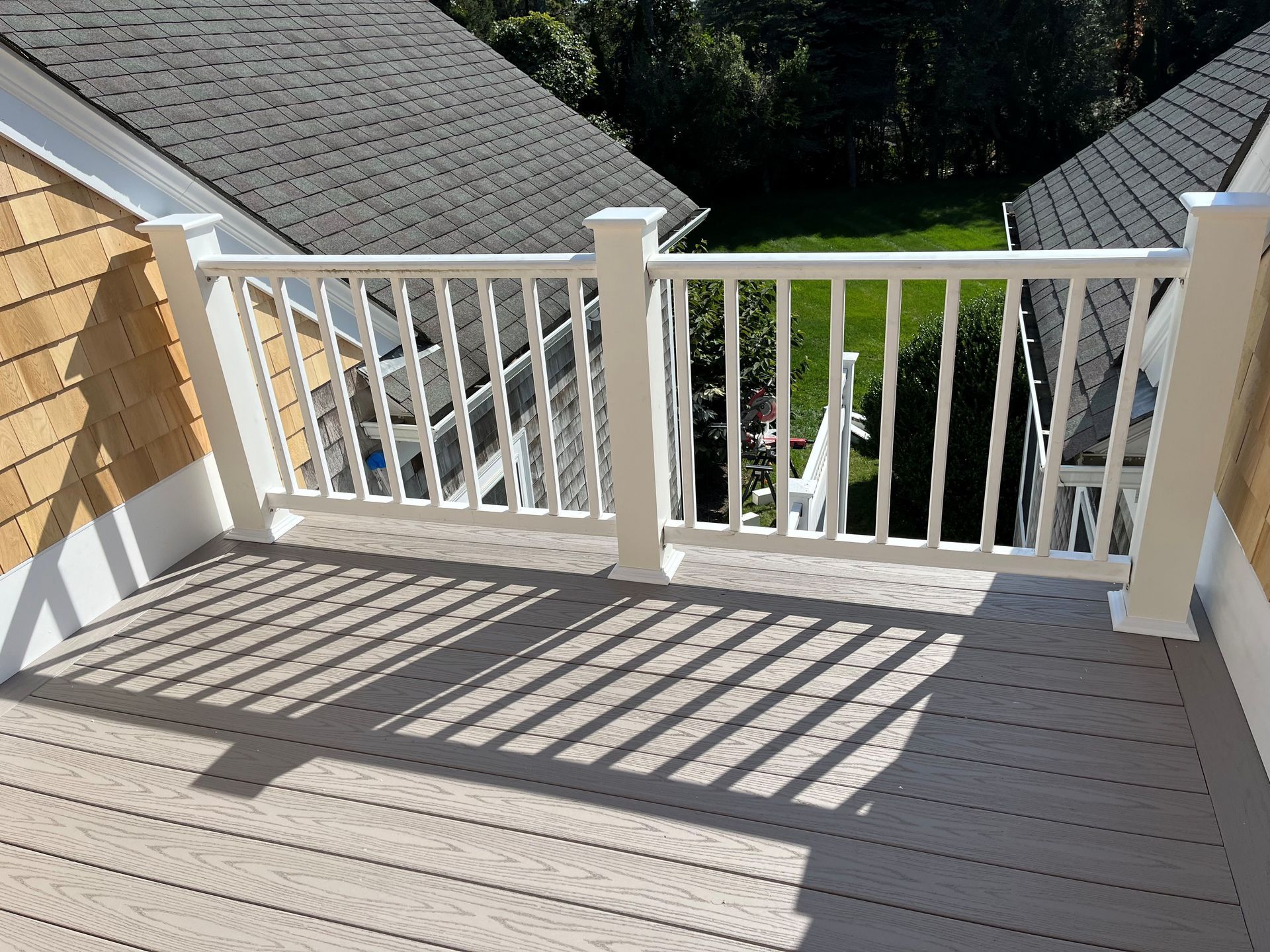 White-railed balcony with gray decking and sunlit shadows overlooking rooftops and greenery