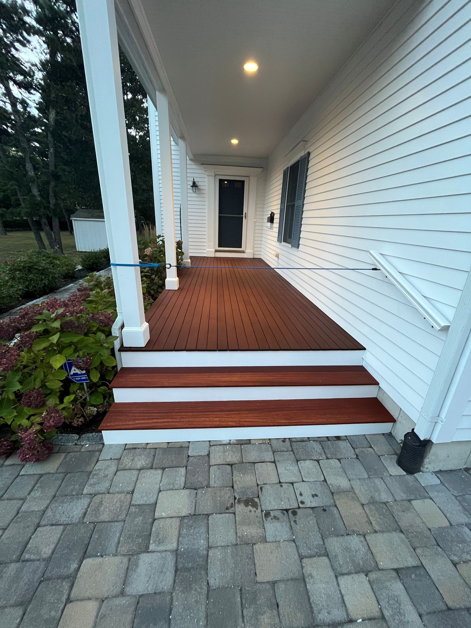 Front porch with white siding, red brick floor, steps, columns, and paver walkway at dusk