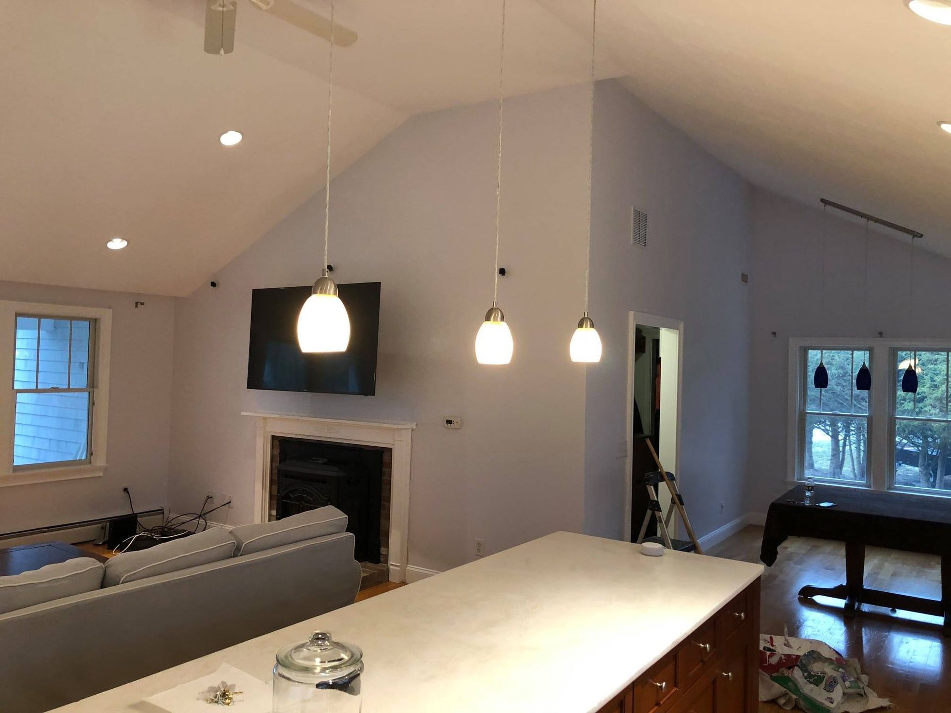 Modern living room with vaulted ceiling, pendant lights, fireplace, TV, and a kitchen island in the foreground