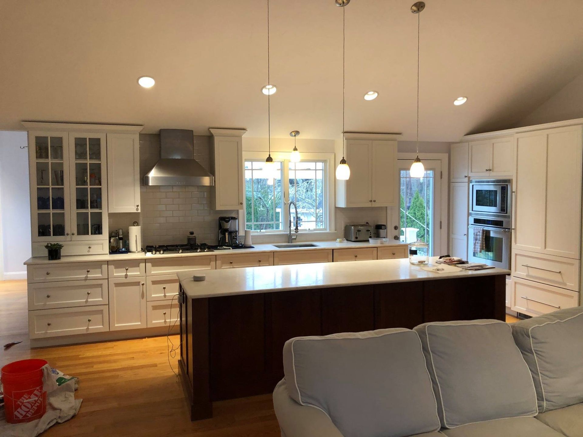 Bright, modern kitchen with white cabinets, large island, pendant lights, and a gray sofa in the foreground