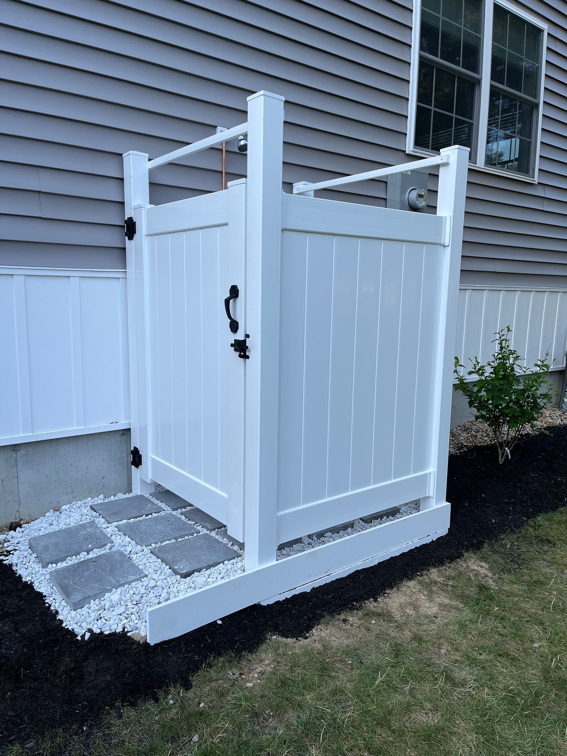 White accessible outdoor shower with ramp and privacy panels beside a house