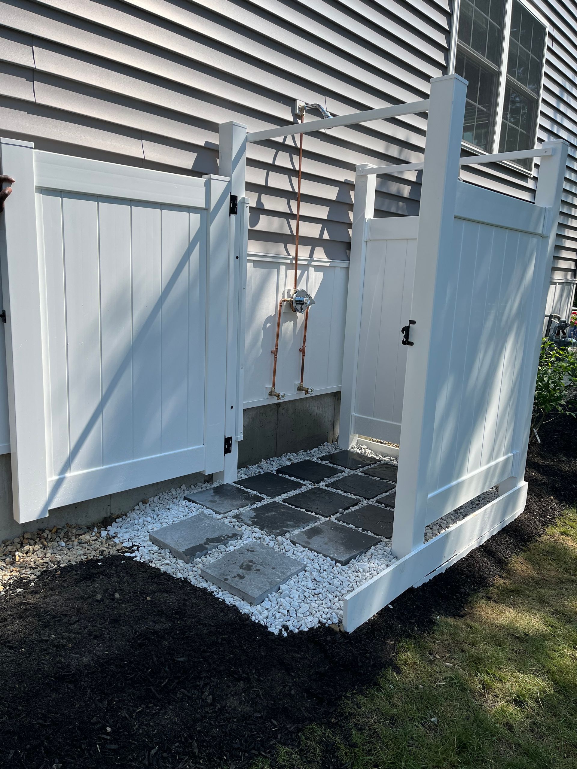 Open white gate in a fenced backyard with a tiled pet wash area and ramp leading inside the enclosure