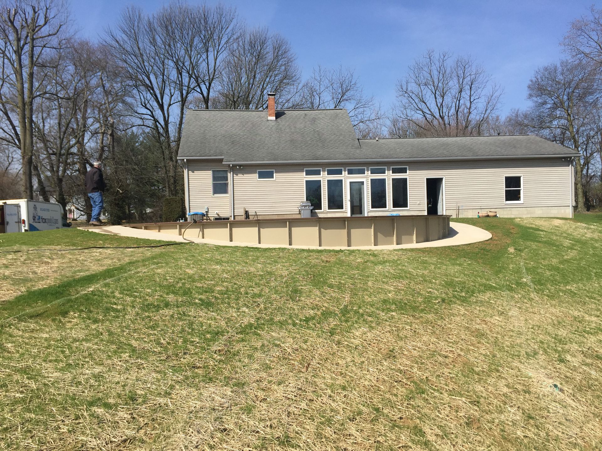 A man is standing in front of a house with a pool in the backyard.