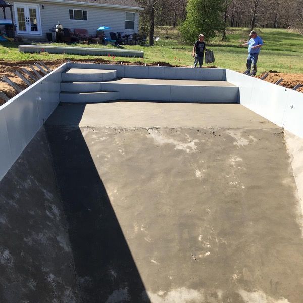 Two men are standing in front of a swimming pool that is being built