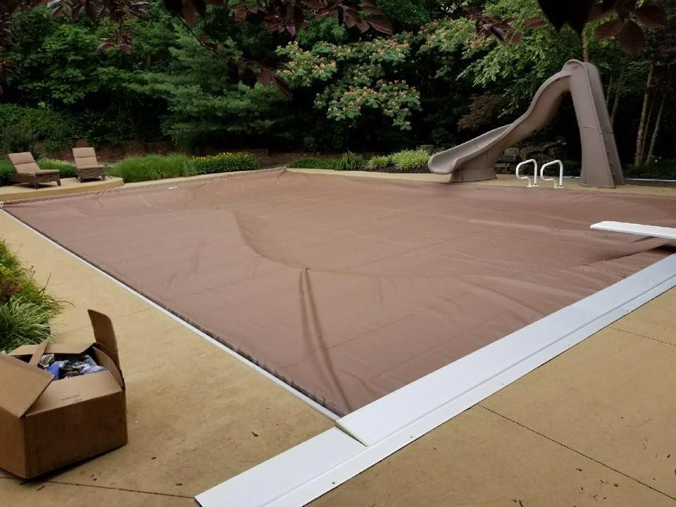 A brown tarp is covering a swimming pool with a slide in the background.