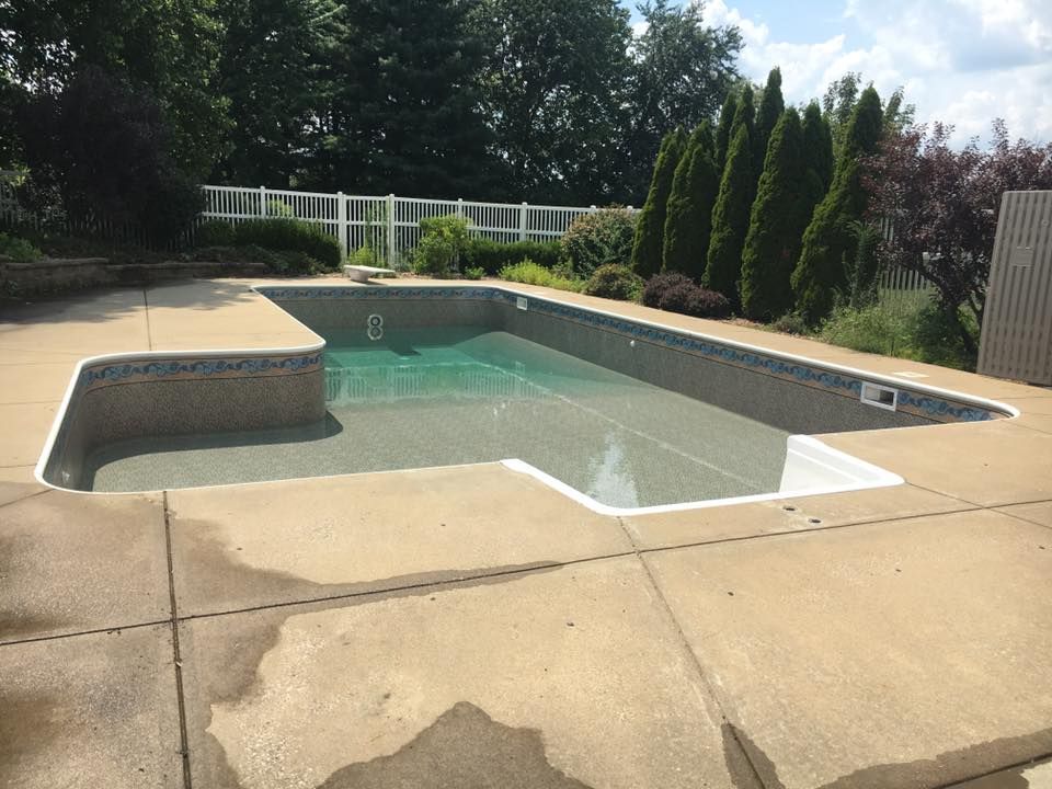 A large swimming pool is surrounded by trees and a fence.