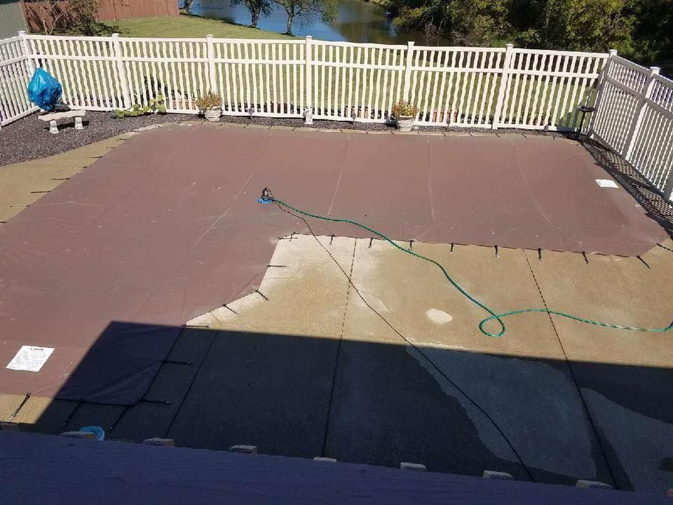 A fence surrounds a swimming pool with a hose attached to it.