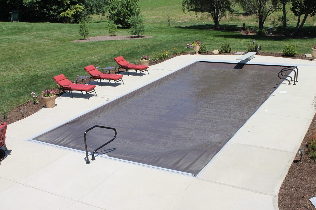A large swimming pool with a cover on it and chairs around it.