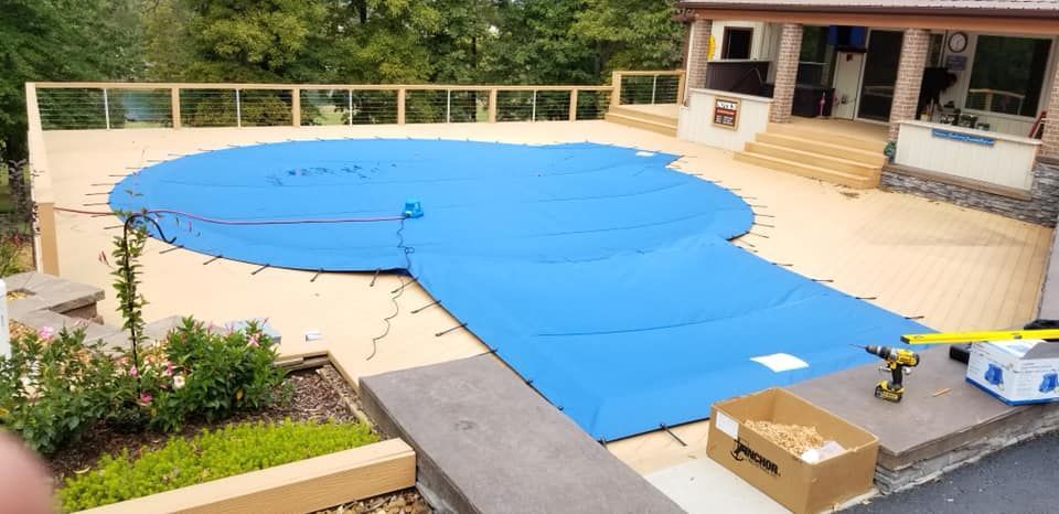 A large swimming pool is being covered with a blue cover.